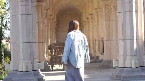 Wallpaper Mural Woman Cemetery Entrance Stone Building - A woman in a blue shirt walks towards the entrance of a cemetery, passing through a stone archway with columns. Torontodigital.ca