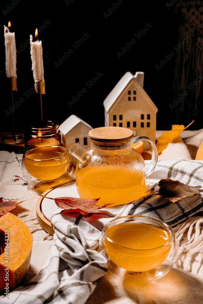 Fototapeta premium Warm autumn composition with glass teapot of steaming pumpkin tea, candles and fall decor. Cozy lifestyle concept.