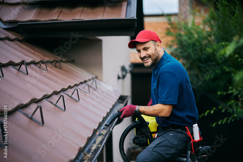 Bilde på lerret Happy maintenance worker cleaning gutters on roof with blower.