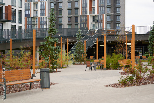 modern urban courtyard features benches, potted trees, and string lights creating inviting public space in residential complex. open area encourages community interaction and relaxation