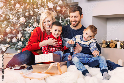 Cheerful family with mother and father and two sons open gift boxes for christmas while sitting on the floor