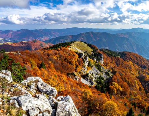 Vivid autumn foliage covers mountain ridges under a partly cloudy sky