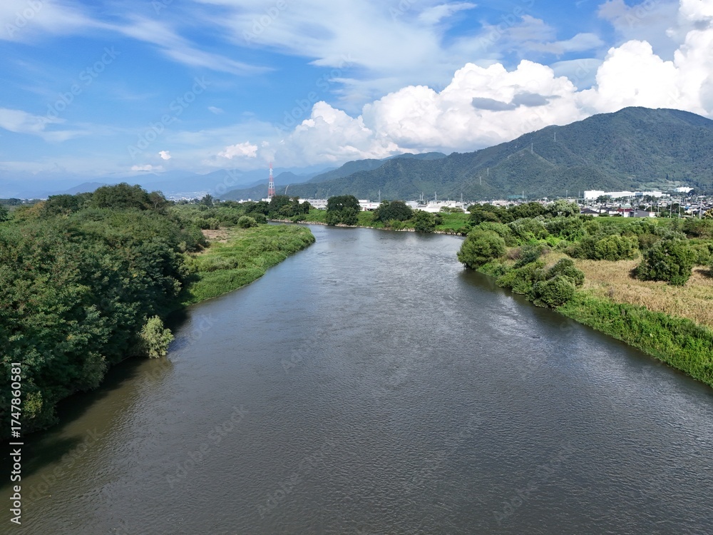 Fototapeta premium A bridge spans a river in a lush green valley. The bridge is surrounded by trees and the valley is full of greenery