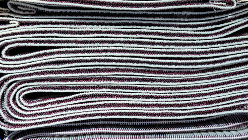 Close up of Rolled Textile Material with Patterned Design on a Shelf. A stack of traditional Indonesian woven fabrics textiles in variety colors and textures are neatly arranged in store display.
