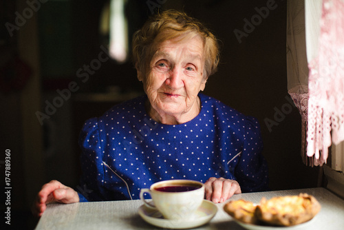 Bilde på lerret An elderly grandmother sits at a table with a cup of tea, her face calm and kind