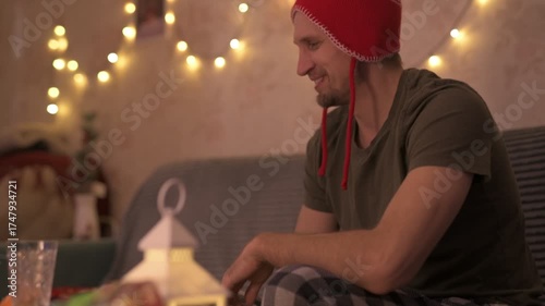 A young man in a red New Year's hat celebrates Christmas alone at home