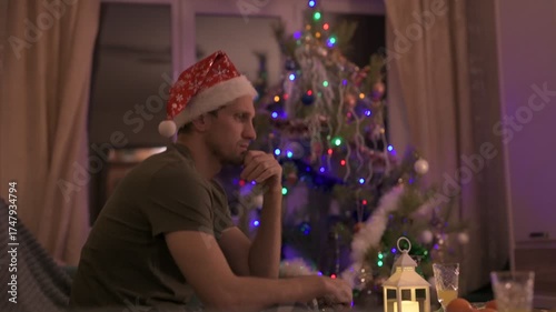 A young man in a red New Year's hat celebrates Christmas alone at home