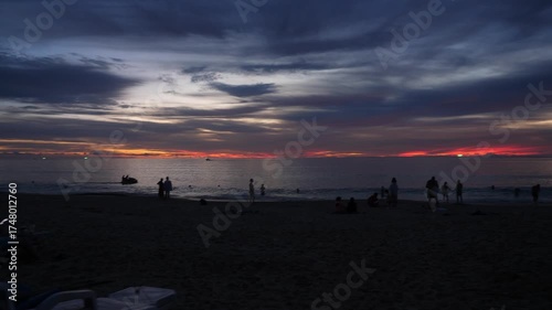 Breathtaking Red Sunset on Thailand Beach - People Relaxing on Shore with Ocean Waves . Stunning ground-level shot of a vibrant red sunset over a tropical beach in Thailand