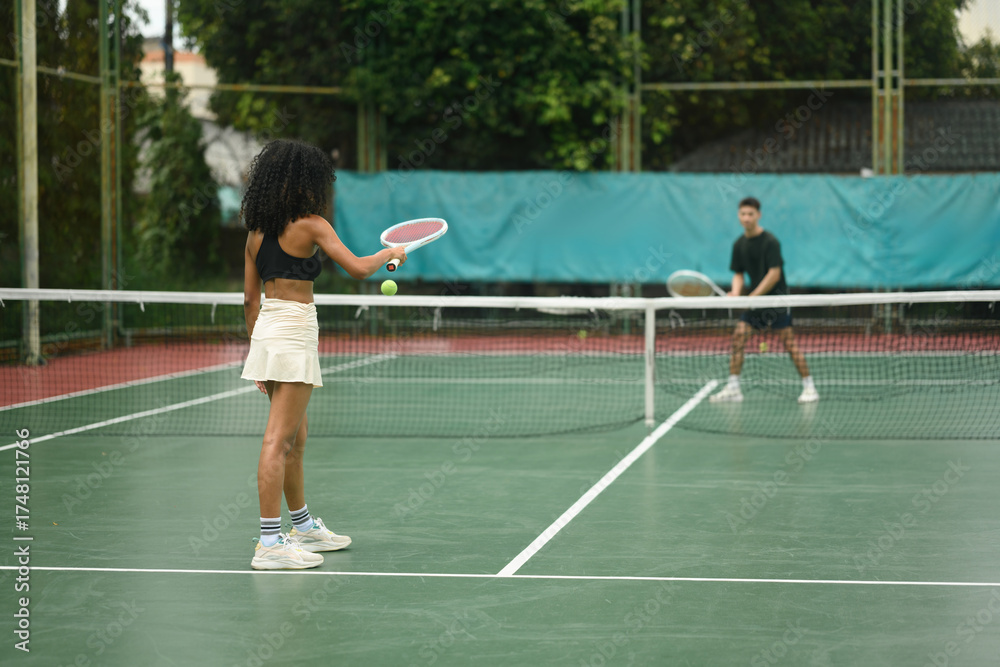 Obraz premium African woman prepares to serve against Asian opponent during a mixed tennis match, symbolizing diversity and competition