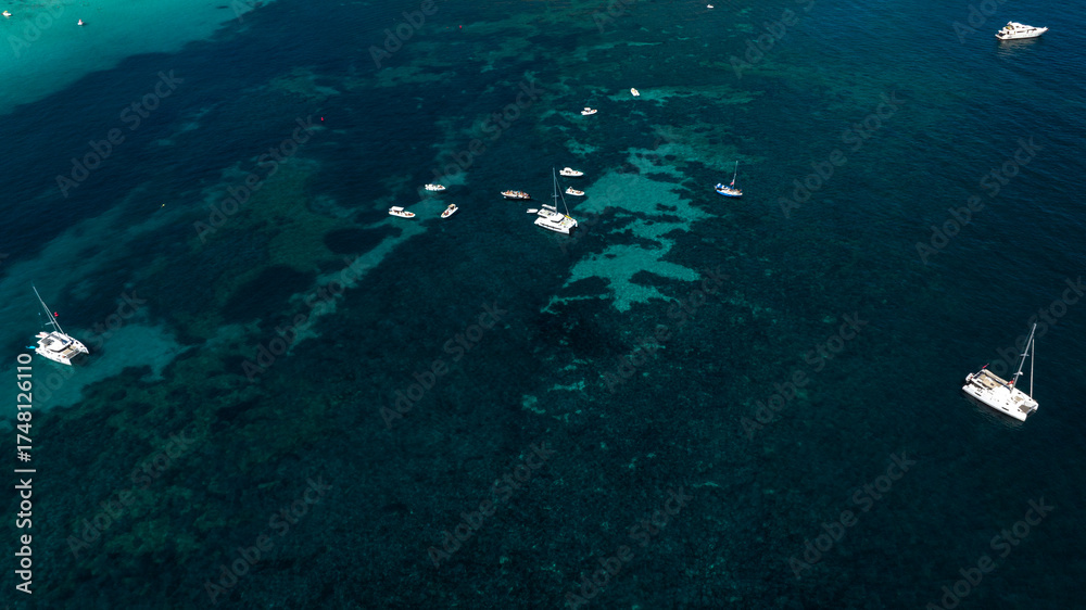 Fototapeta premium Aerial view of boats offshore in a bay with crystal-clear water. The water is calm and the colors range from azure to turquoise.