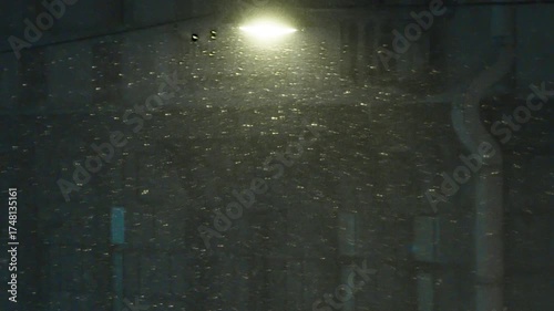 Snowfall and Street Lighting. In the light of a street lamp, snowflakes of a heavy snowfall fly by. In the background, the dark facade of a night building