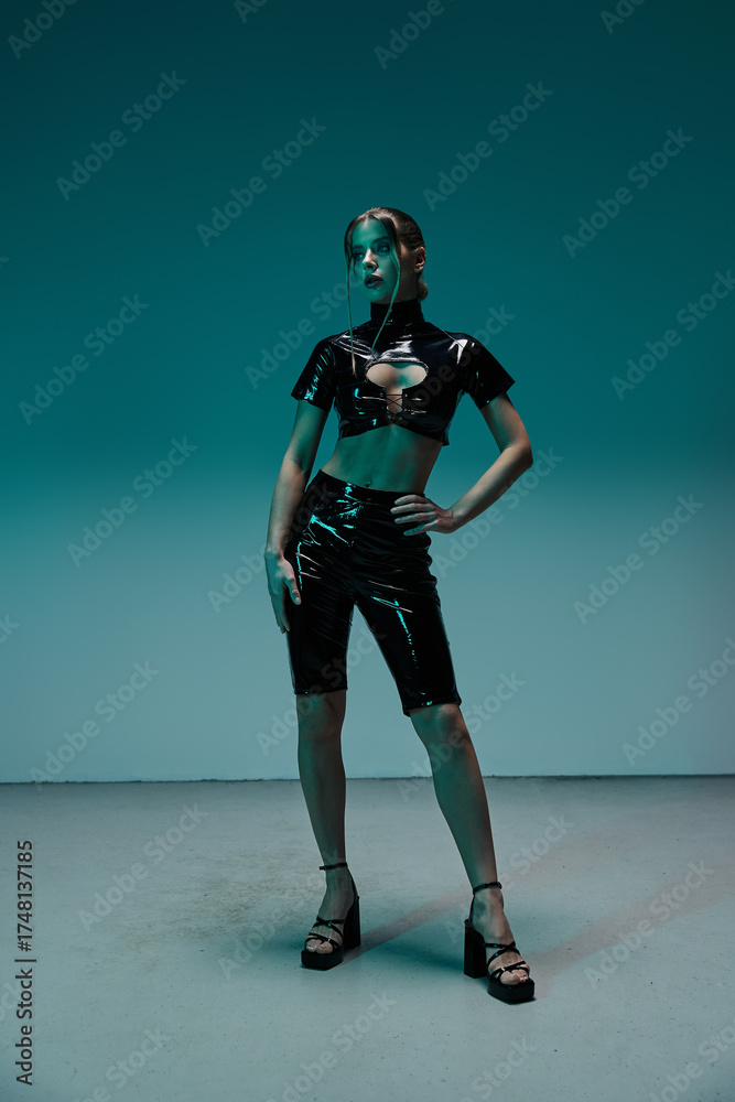 Fototapeta premium Seductive young woman confidently showcases stylish black latex outfit in studio setting