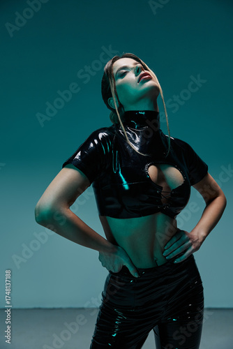 Quadro su tela Seductive young woman poses confidently in stylish black latex outfit in studio