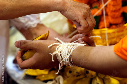 Buddhist ceremony at Wat May Souvannapoumaram temple. Monk ties blessed cotton bracetet ( Sai-sin) around a wrist. Luang Prabang. Laos.