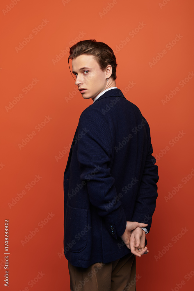 Fototapeta premium Stylish young man poses confidently against vibrant orange background in modern youth culture scene