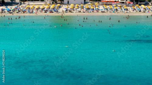 Aerial view of Mondello Beach, located near Palermo, Sicily, Italy. There are many people on holiday in the bay. The Mediterranean Sea is emerald and crystal clear.