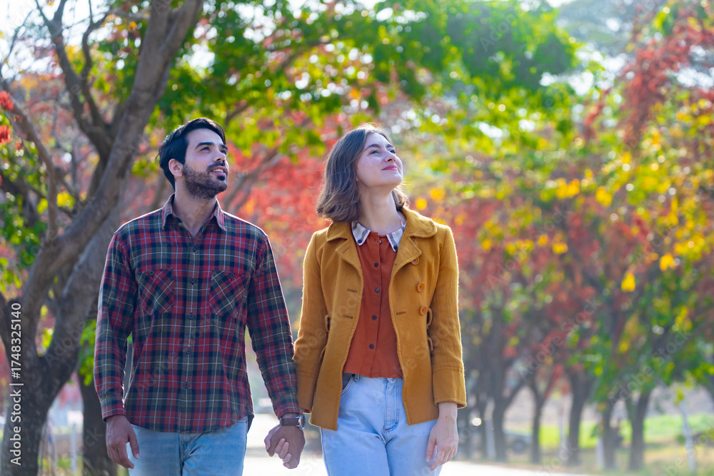 Naklejka premium Happy caucasian couple walking together in the public park during autumn with maple and beech tree for fall color travel destination and family happiness