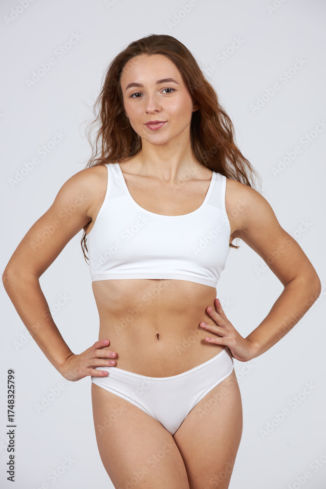 Fototapeta premium Young beautiful girl in white lingerie with loose hair on a gray background