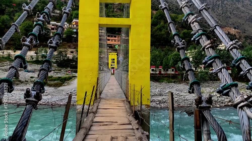 A panoramic view and close-up perspective of a vibrant yellow suspension bridge crossing the turquoise Swat River, framed by the lush, towering mountains of Khyber Pakhtunkhwa, Pakistan.