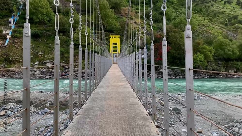 A panoramic view and close-up perspective of a vibrant yellow suspension bridge crossing the turquoise Swat River, framed by the lush, towering mountains of Khyber Pakhtunkhwa, Pakistan.
