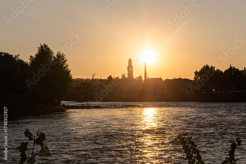 A classic European sunset scene. The skyline of a charming village, with its bell tower and bridge, is cast in shadow by the brilliant setting sun.