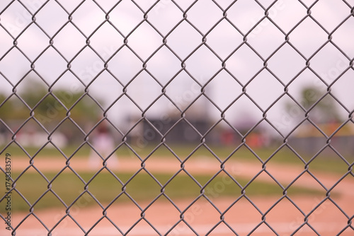 Chain link fence in focus with a baseball field in the blurry background