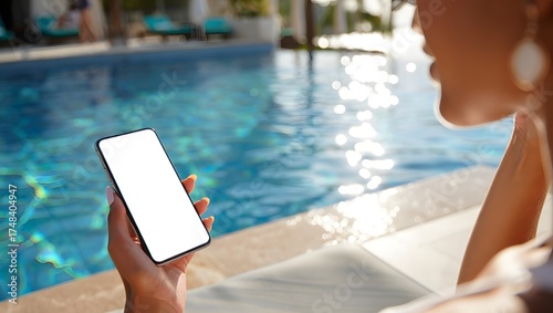 photograph of a beautiful young woman relaxing beside a luxury infinity pool, elegantly holding a mobile smartphone with a bright white screen