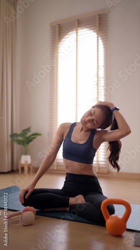 Asian adult woman stretching neck on yoga mat home fitness routine wellness exercise indoor morning workout healthy living
