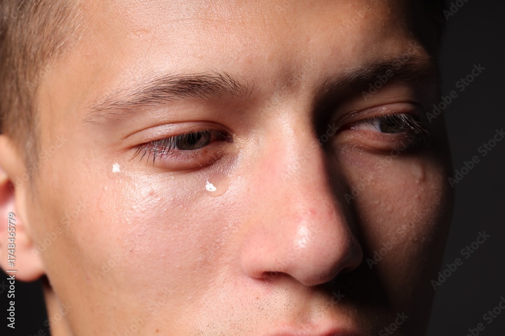 Fototapeta premium Sad man crying on black background, closeup