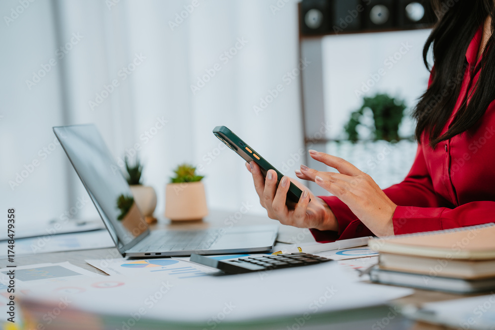 Fototapeta premium Smiling businesswoman talking on phone and holding tablet while working with documents and laptop in office