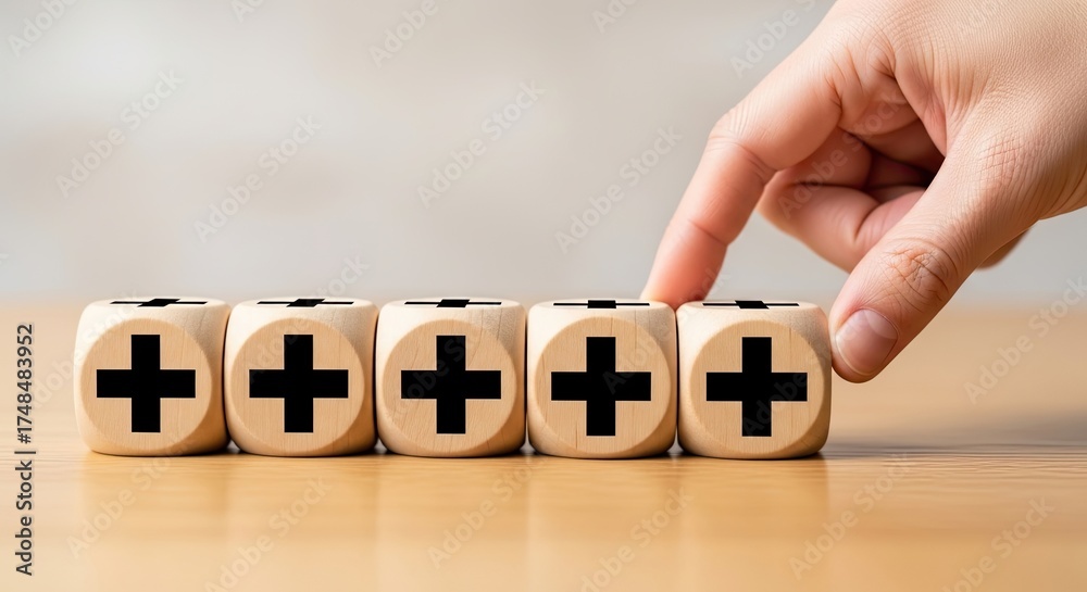 Fototapeta premium Hand Arranging Five Wood Dice Cubes Displaying Black Plus Signs on Light Brown Tabletop