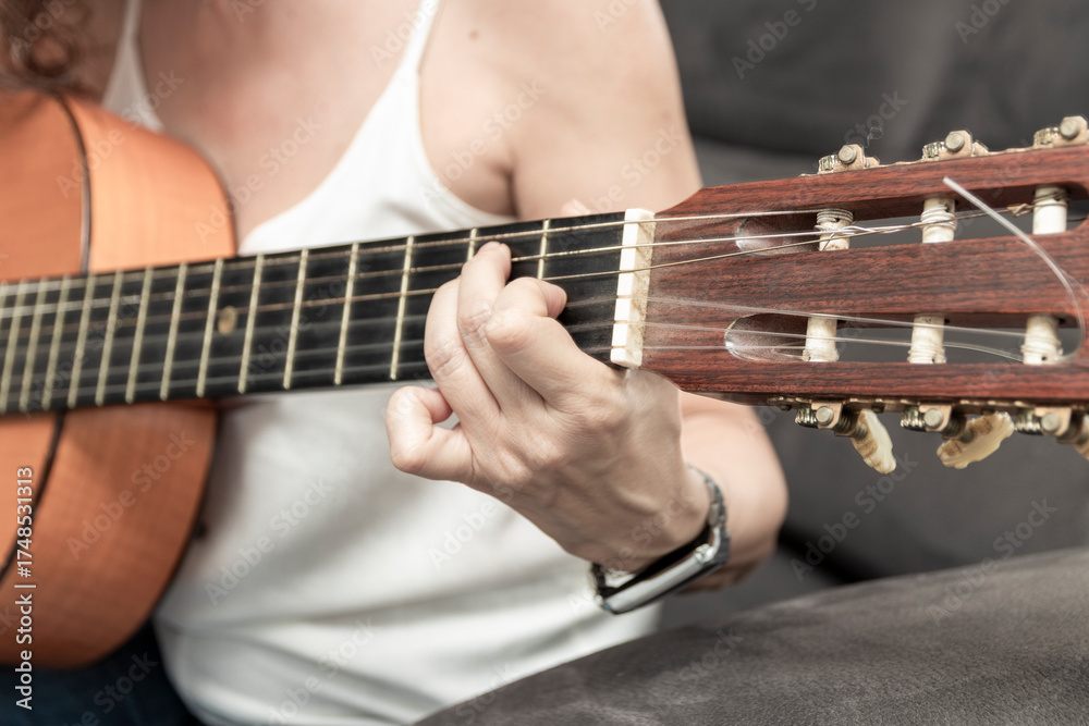 Obraz premium Woman playing classical guitar, pressing chords on fretboard