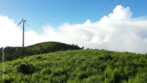 Wind Turbine on Lush Green Hill Under Blue Sky and White Clouds with Clean Energy Landscape and Renewable Power Generation in Environmental Scenery