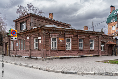 Wooden residential house from 1892 with carved details and white windows under an overcast sky. Historic structure in an urban setting showing signs of wear.