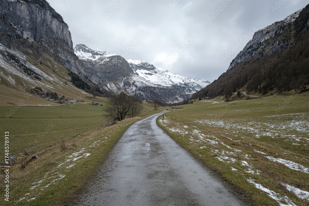 Fototapeta premium Scenic mountain road winding through snow-capped peaks and green fields in early spring