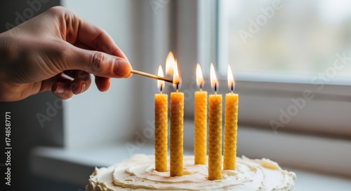 Hand lighting five candles on a birthday cake by a window