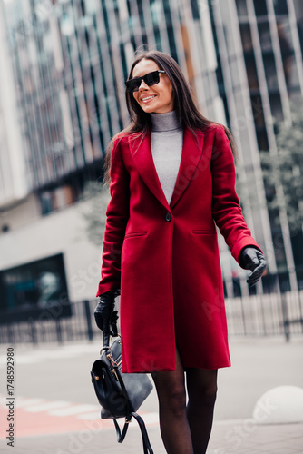 Confident woman wearing red coat and sunglass walking stylishly in urban setting with high fashion chic