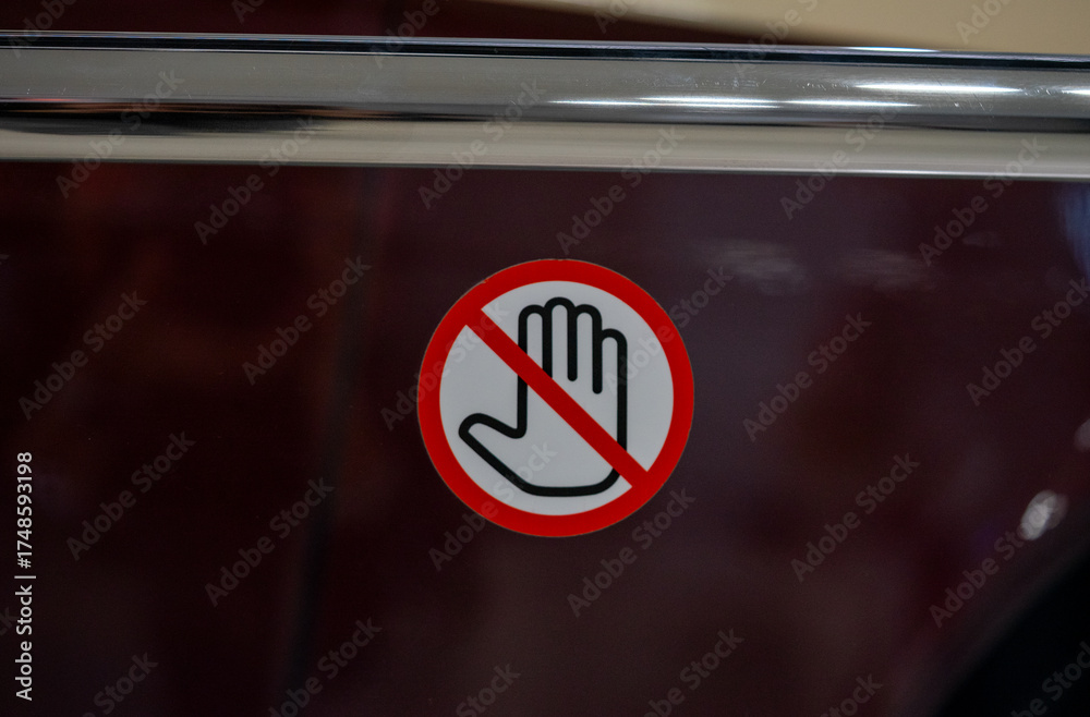 Obraz premium Warning sign featuring a hand symbol crossed out, indicating restricted access or no entry. Placed on a horizontal metal bar, the sign symbolizes caution and restriction. 