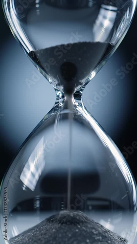 Extreme close-up macro zoom video of an exquisite borosilicate glass hourglass with obsidian sand falling, against a dark indigo gradient with bokeh. Tranquil passage of time concept