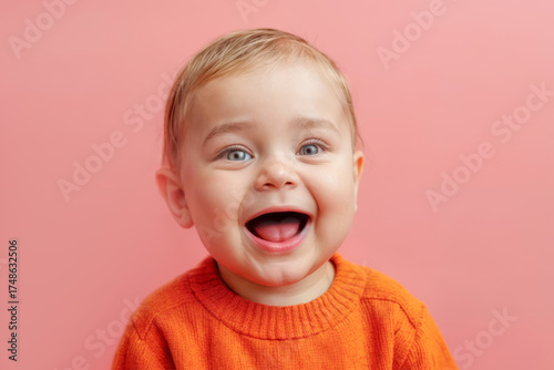 Happy baby with bright blue eyes and a big smile wearing an orange sweater against a pink background