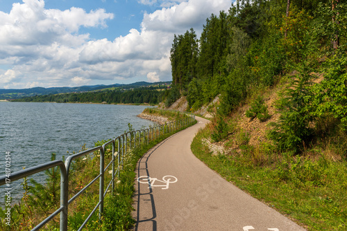 Wallpaper Mural Smooth paved cycling path curves along the lakeshore, framed by lush forest and distant hills. Ideal concept for active travel, nature recreation, and outdoor freedom. Torontodigital.ca