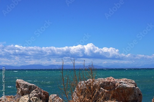 A view of the sea, clouds, rocks and the island of Aegina, on a windy day, from a beach in Glyfada, Greece
