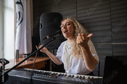 Fotografie Caucasian woman singing into microphone and playing synthesizer and recording herself on laptop
