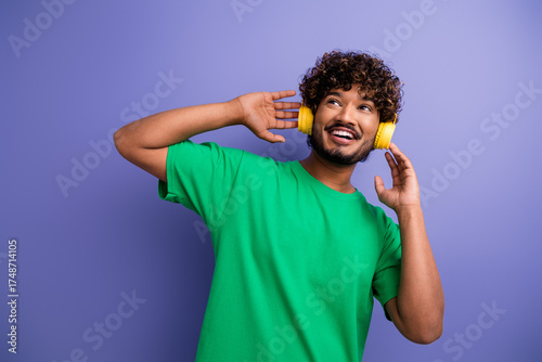 Schilderij op canvas Positive man in a green T-shirt enjoying music with yellow headphones, posing ex