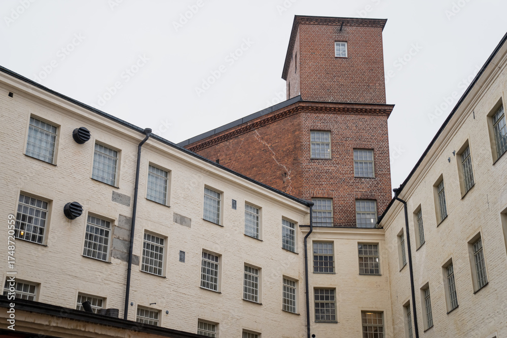 Obraz premium Historic industrial architecture in Tampere Finland with red brick tower and white plaster factory walls representing preserved industrial heritage, adaptive reuse design, and Nordic urban buildings