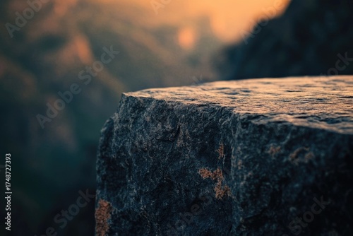 Close-up of a textured dark rock edge, illuminated by a warm glow, set against a soft, blurred, atmospheric background.