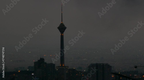 Wallpaper Mural Milad Tower rises against a dark cloudy night in Tehran, its lights glowing above the cityscape, a dramatic cinematic shot blending urban life and mystery. Torontodigital.ca