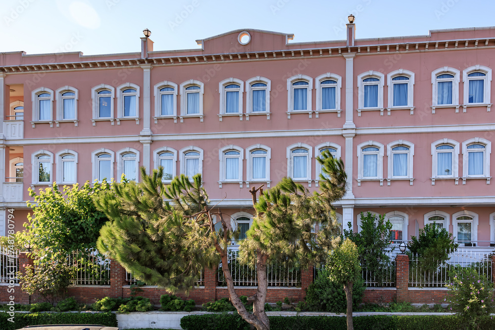Fototapeta premium Elegant pink building with symmetrical windows and lush greenery in urban setting