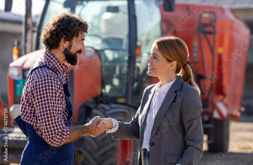 Farmer and businesswoman shaking hands in front of tractor