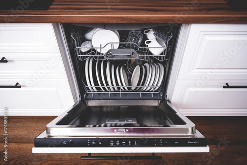 Open built-in dishwasher reveals neatly organized, clean plates and utensils in stylish kitchen with wooden cabinetry